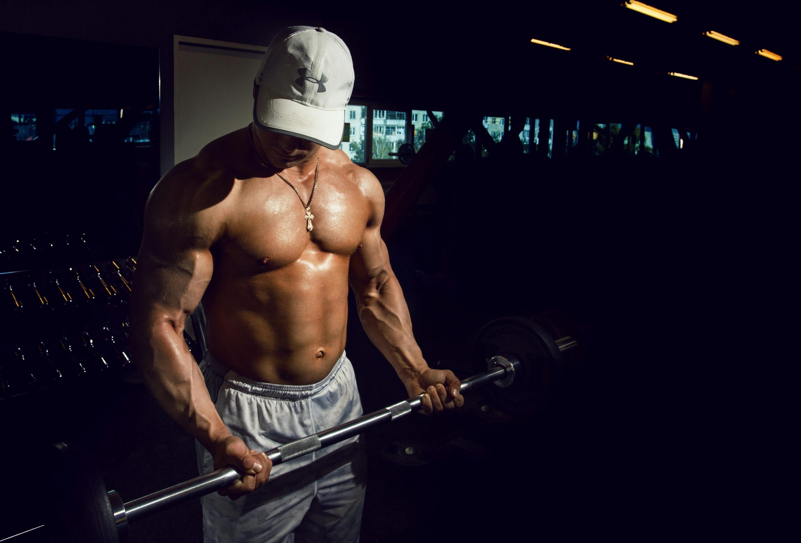 Strong shirtless man lifting barbell in a dimly lit gym, embodying fitness and strength.
